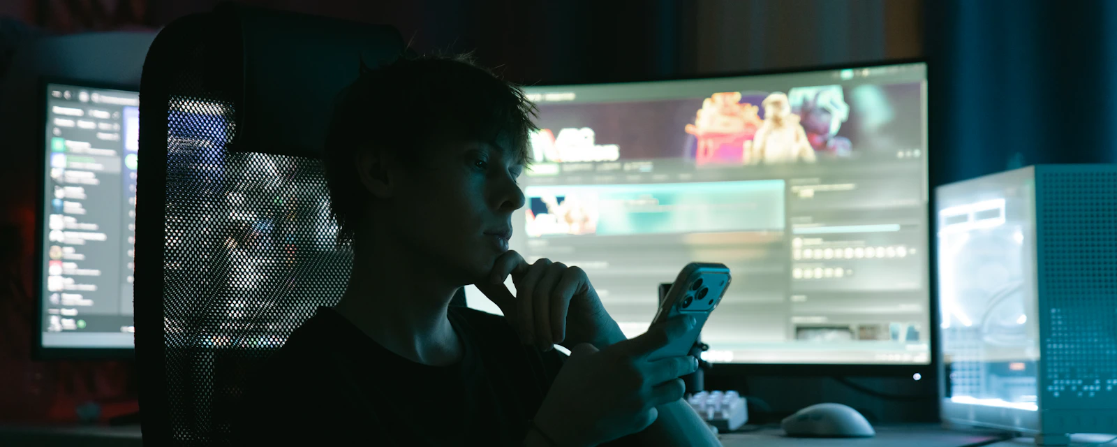 A person checking a phone in front of several monitors